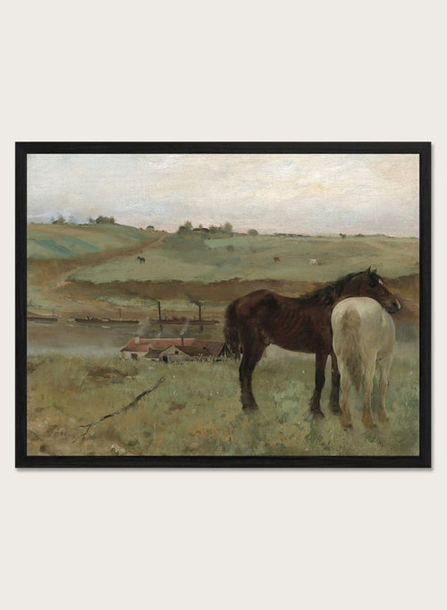 A framed landscape painting depicting two horses in a grassy field, with a muted sky and distant hills. Horses in a Meadow by Edgar Degas is a vintage horse art print featuring two horses standing together in a green field with a river, hills, and distant village.