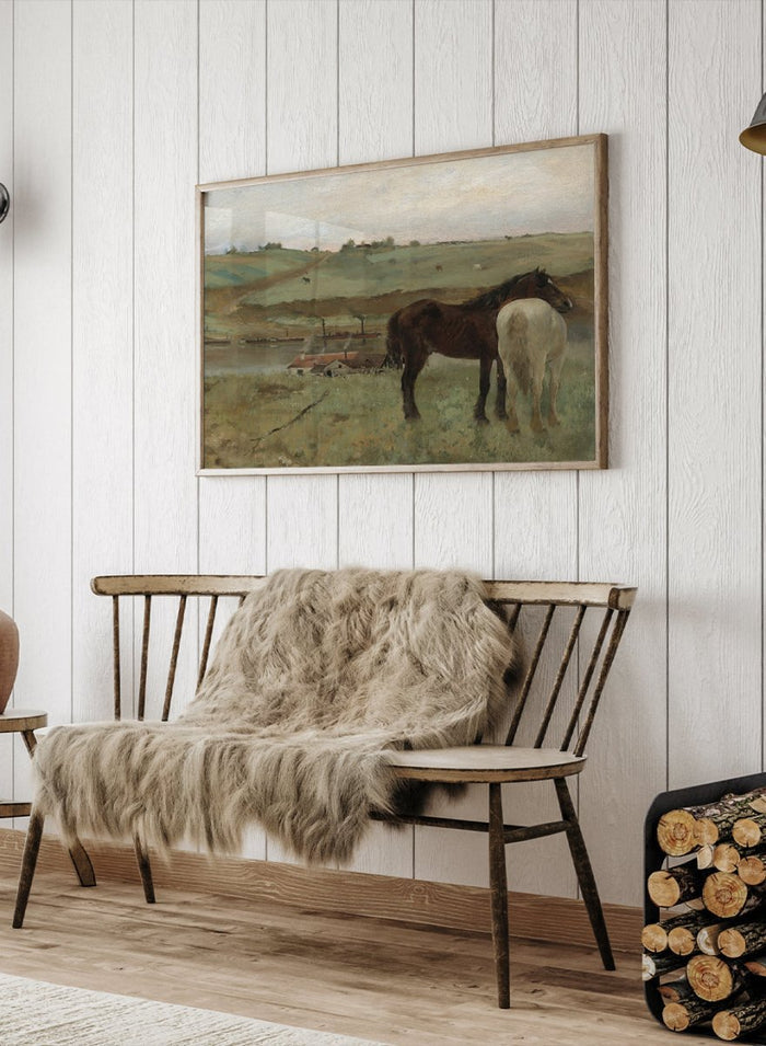 A framed landscape painting depicting two horses in a grassy field, with a muted sky and distant hills. Horses in a Meadow by Edgar Degas is a vintage horse art print featuring two horses standing together in a green field with a river, hills, and distant village.