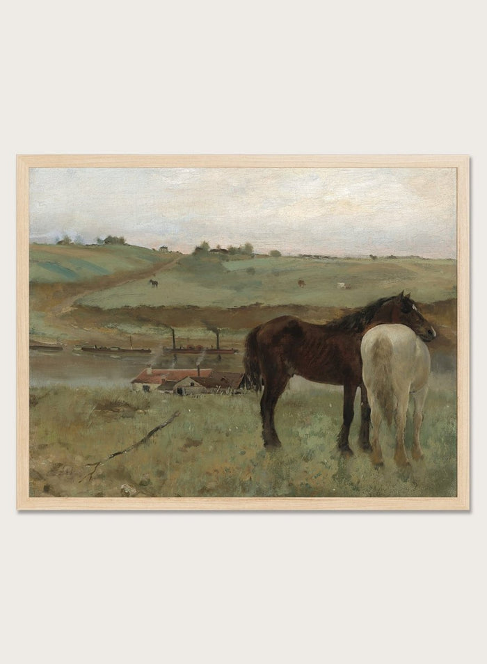 A framed landscape painting depicting two horses in a grassy field, with a muted sky and distant hills. Horses in a Meadow by Edgar Degas is a vintage horse art print featuring two horses standing together in a green field with a river, hills, and distant village.