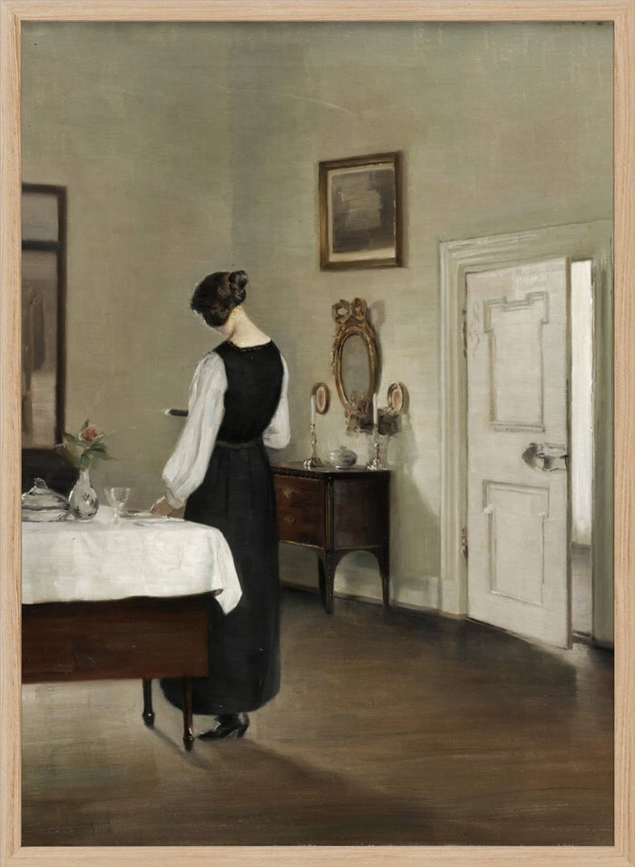Woman in a black dress standing in a room with a table and mirror. In the Dining Room by Carl Holsøe is a vintage Danish interior art print featuring a woman in a softly lit dining room with muted tones and classic Scandinavian style.