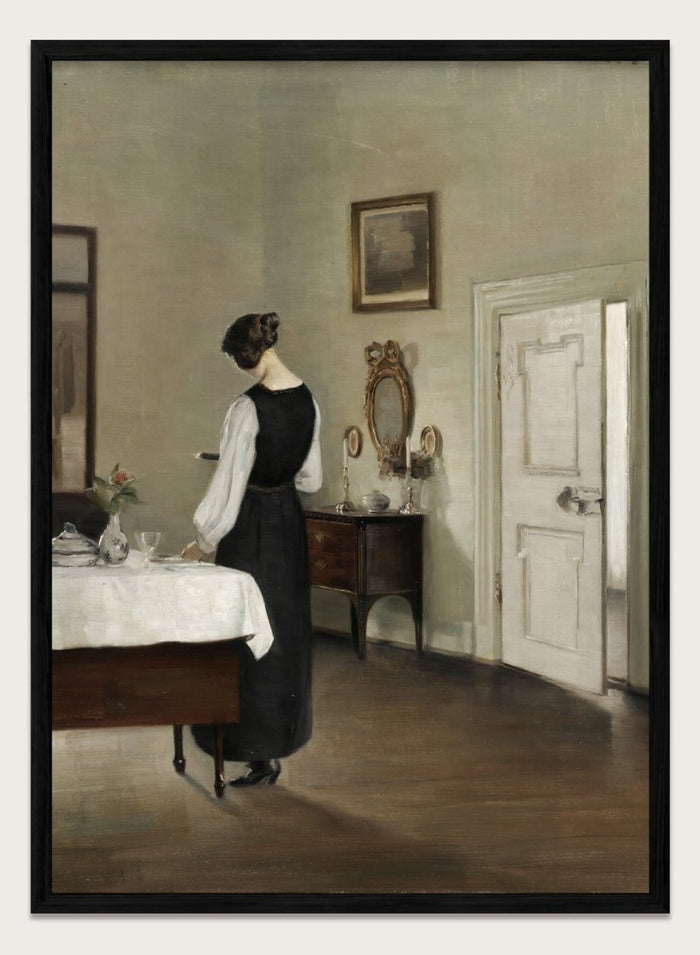 Woman in a black dress standing in a room with a table and mirror. In the Dining Room by Carl Holsøe is a vintage Danish interior art print featuring a woman in a softly lit dining room with muted tones and classic Scandinavian style.