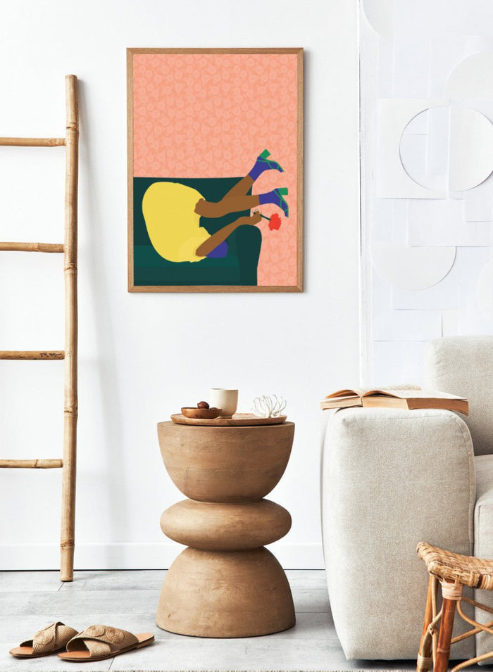 Illustration of a person sitting on a couch with a flower, against a patterned pink background. New Year’s Eve by Jota De Jai is a playful modern fine art print of a woman upside down on a couch in heels and a yellow dress. Available framed or unframed.