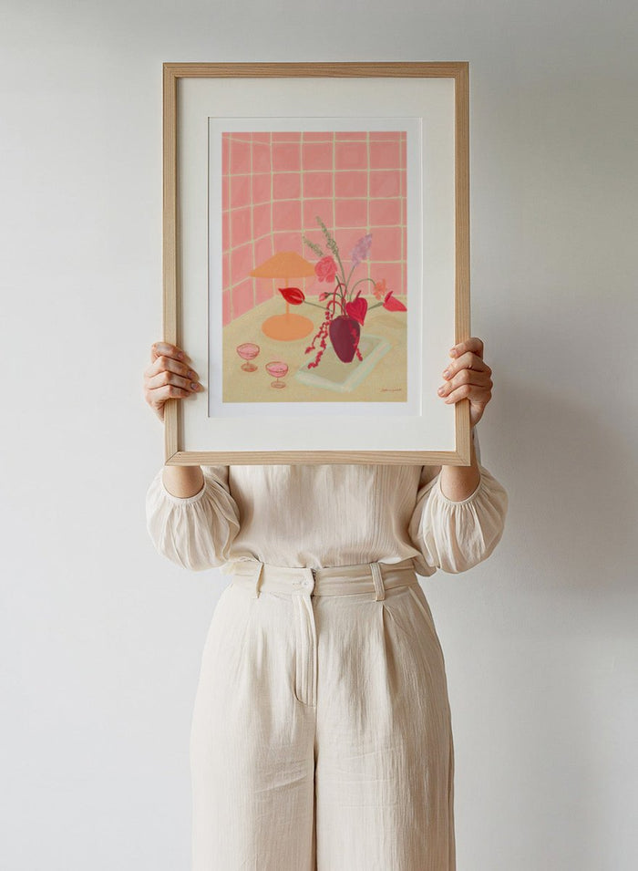 Illustration of a table with a vase of flowers, two glasses, and an orange lamp against a pink tiled wall. Bubbly by Katharina Puritscher art print featuring pink tiled walls, floral still life, coupe glasses, and a cozy tabletop scene. Officially licensed wall poster.