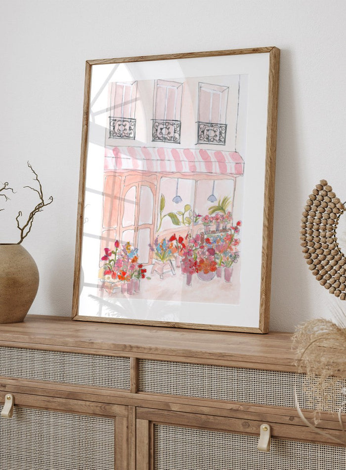 Illustration of a flower shop with a striped awning and flowers in front. Pink Flower Shop by Katharina Puritscher features a Paris-inspired storefront illustration with colorful bouquets, soft watercolor textures, and European street details. Floral art print with optional framing.