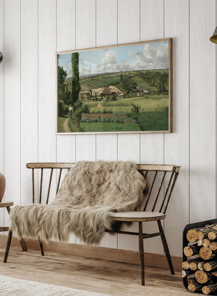 A framed landscape painting depicting a green countryside scene with rolling hills, trees, a path, small buildings, and a cloudy sky. Landscape at Les Pâtis, Pontoise by Camille Pissarro is a vintage French landscape print featuring green fields, farm workers, rolling hills, and a summer sky.