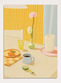 A stylized illustration of a tabletop scene with a pink flower in a small green vase, a yellow patterned glass, a white mug on a pink saucer, a gray mug of coffee, a sliced lime, and an orange on a checkered mat against a yellow tiled wall. Bright Breakfast Table by Lisa Solomoniuk premium framed fine art print featuring morning coffee, citrus fruit, flowers, and colorful tableware.
