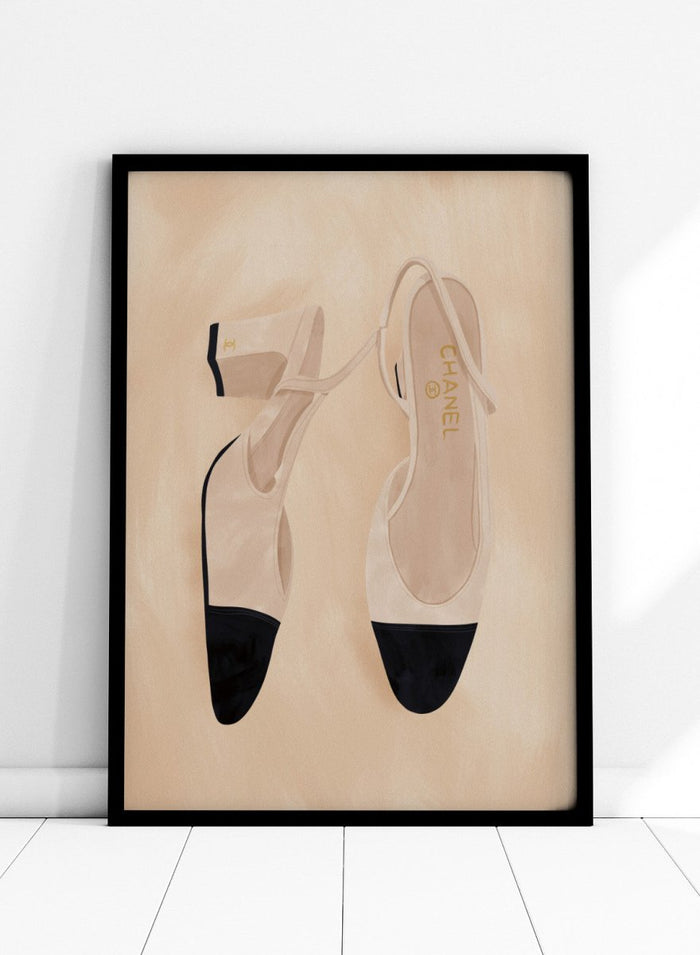 A pair of slingback flats with a beige and black color-blocked design, displayed on a textured beige background with a black border. Chic Cap-Toe Heels by Lisa Solomoniuk premium framed fine art print featuring cream slingback heels with black cap toes on a soft beige background.