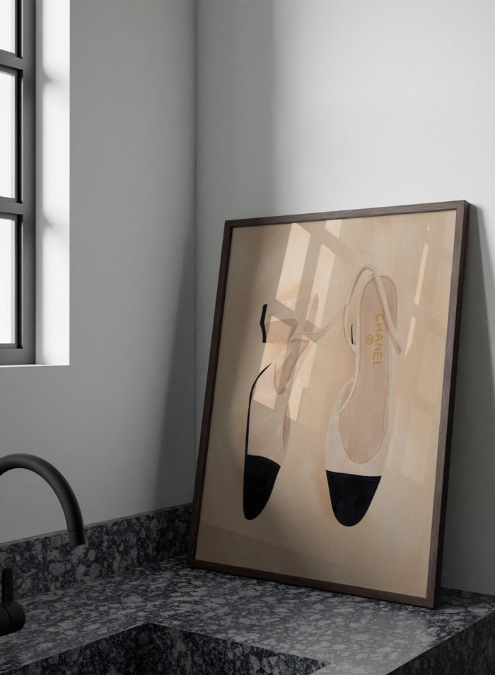A pair of slingback flats with a beige and black color-blocked design, displayed on a textured beige background with a black border. Chic Cap-Toe Heels by Lisa Solomoniuk premium framed fine art print featuring cream slingback heels with black cap toes on a soft beige background.
