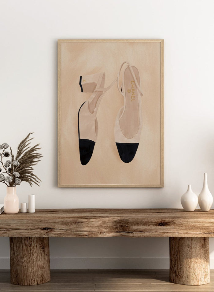 A pair of slingback flats with a beige and black color-blocked design, displayed on a textured beige background with a black border. Chic Cap-Toe Heels by Lisa Solomoniuk premium framed fine art print featuring cream slingback heels with black cap toes on a soft beige background.