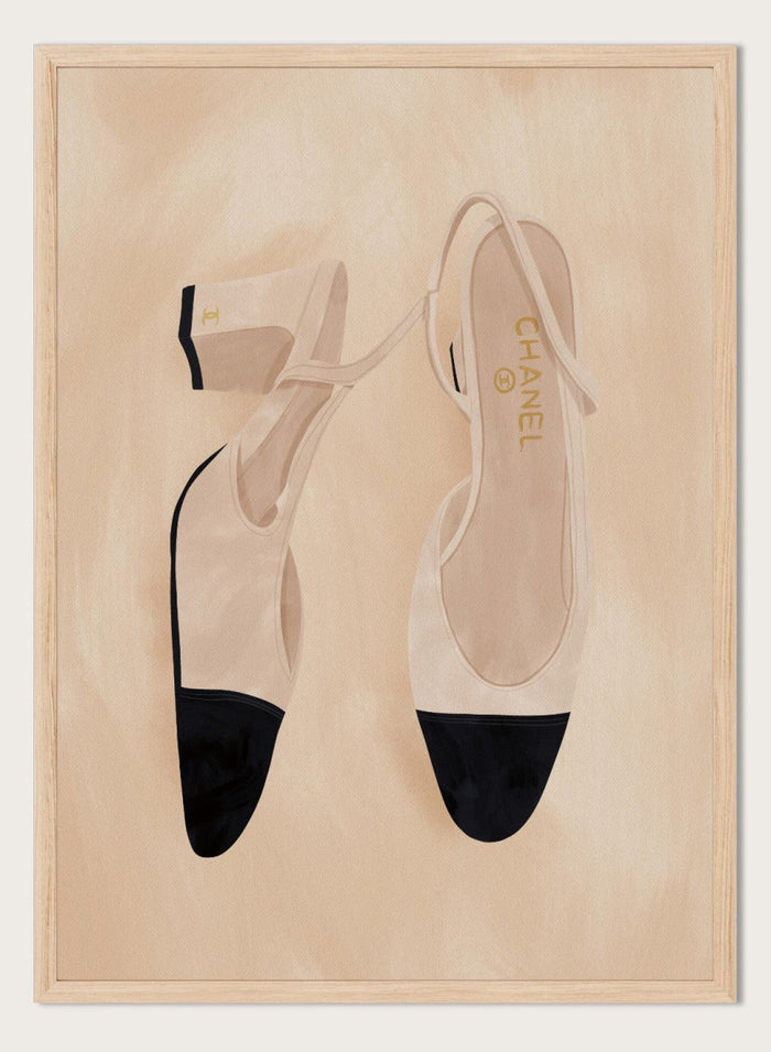 A pair of slingback flats with a beige and black color-blocked design, displayed on a textured beige background with a black border. Chic Cap-Toe Heels by Lisa Solomoniuk premium framed fine art print featuring cream slingback heels with black cap toes on a soft beige background.