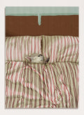 A cozy bed setup with beige and red striped bedding, two matching pillows, and a small gray cat curled up on the duvet. The background features a brown textured headboard and a mint green wall at the top. Shop Cozy Dog in Bed by Lisa Solomoniuk, a playful dog animal art print featuring a pup tucked into striped bedding with a warm, cozy bedroom feel.