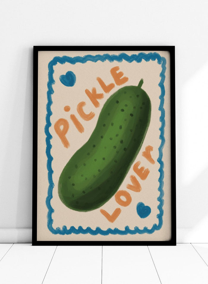 An art print featuring a hand-drawn green pickle centered on a cream background, surrounded by a blue scalloped border. The words 'PICKLE' and 'LOVER' appear in orange lettering, with two small blue hearts near the corners. Cute Pickle Lover by Lisa Solomoniuk premium framed fine art print featuring a giant green pickle, playful lettering, blue hearts, and a hand-painted border.