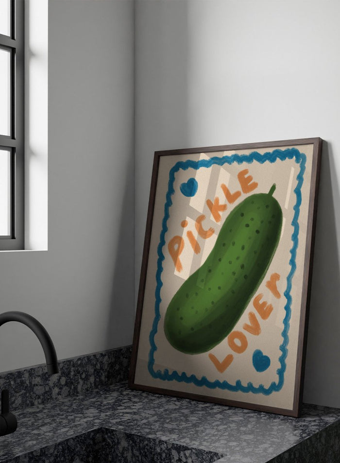 An art print featuring a hand-drawn green pickle centered on a cream background, surrounded by a blue scalloped border. The words 'PICKLE' and 'LOVER' appear in orange lettering, with two small blue hearts near the corners. Cute Pickle Lover by Lisa Solomoniuk premium framed fine art print featuring a giant green pickle, playful lettering, blue hearts, and a hand-painted border.