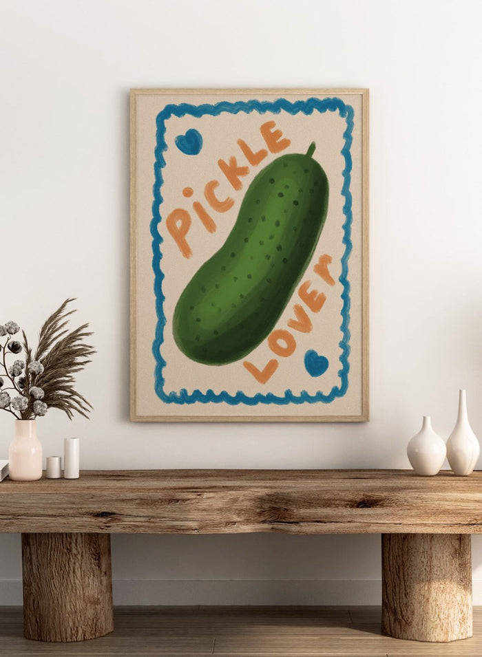 An art print featuring a hand-drawn green pickle centered on a cream background, surrounded by a blue scalloped border. The words 'PICKLE' and 'LOVER' appear in orange lettering, with two small blue hearts near the corners. Cute Pickle Lover by Lisa Solomoniuk premium framed fine art print featuring a giant green pickle, playful lettering, blue hearts, and a hand-painted border.