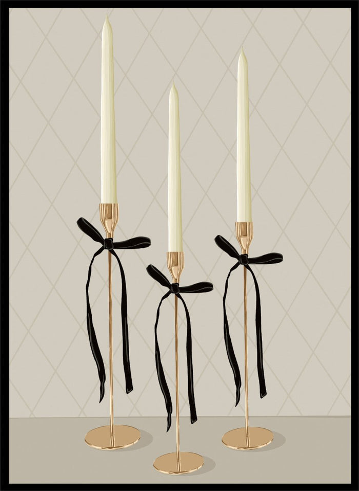 Three gold taper candle holders with cream candles and black ribbon bows, arranged on a light gray surface against a beige diamond-patterned background. Elegant Gold Taper Candles by Lisa Solomoniuk premium framed fine art print featuring gold candlesticks, cream tapers, and long black ribbons.