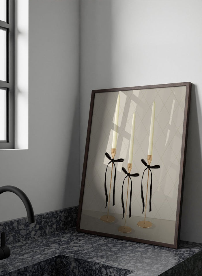 Three gold taper candle holders with cream candles and black ribbon bows, arranged on a light gray surface against a beige diamond-patterned background. Elegant Gold Taper Candles by Lisa Solomoniuk premium framed fine art print featuring gold candlesticks, cream tapers, and long black ribbons.