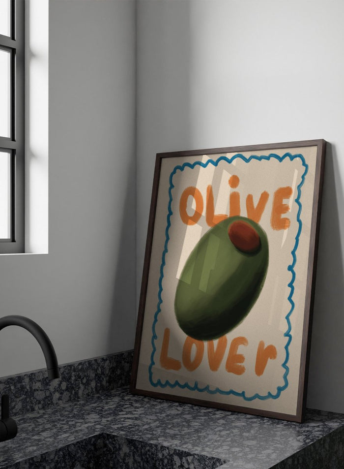 An art print featuring a stylized illustration of an olive with the words 'OLIVE' at the top and 'LOVE' at the bottom, framed by a blue scalloped border on a cream background. Green Olive Lover by Lisa Solomoniuk premium framed fine art print featuring an oversized green olive, orange lettering, and a playful blue border.