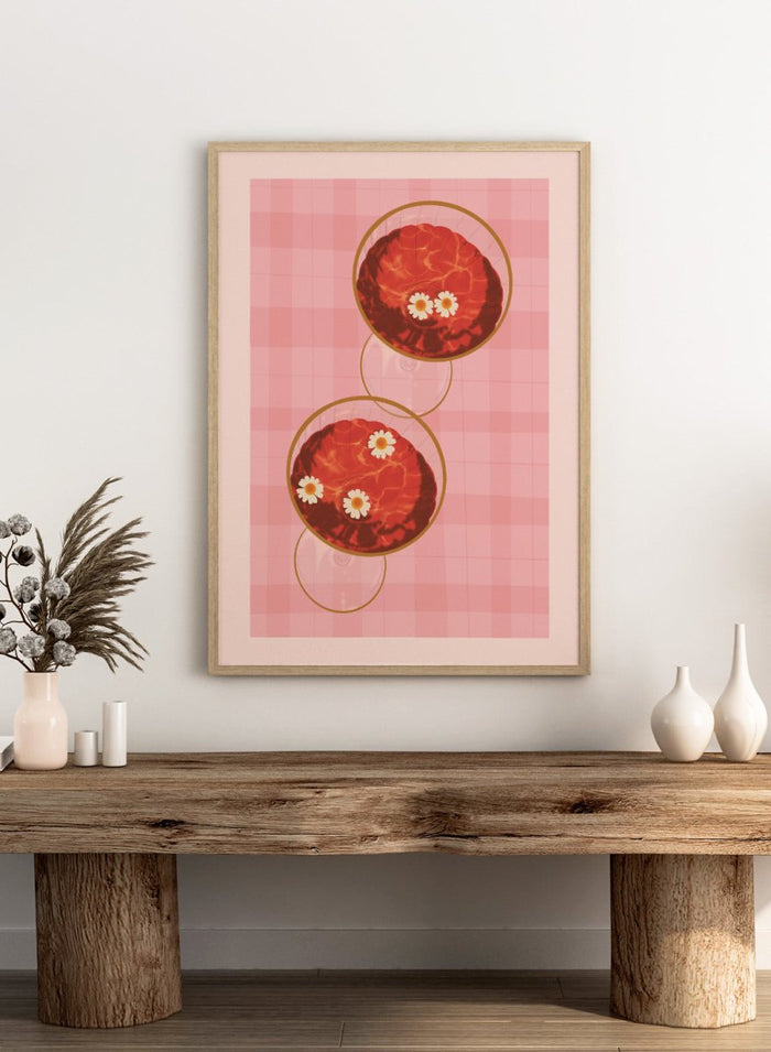 A stylized art print featuring two overlapping pink and red plaid glasses with white daisy flowers, framed by a black border on a light pink background. Pink Drinks With Daisies by Lisa Solomoniuk premium framed fine art print featuring red coupe glasses, floating daisies, and pink gingham.