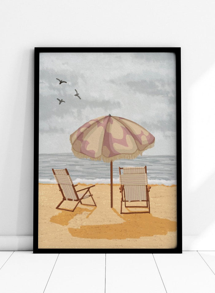 A beach scene artwork showing two wooden deck chairs under a beige and dusty pink patterned umbrella on a sandy shore, with the ocean and cloudy sky behind them. Two birds are visible in the sky. Seaside Umbrella Chairs by Lisa Solomoniuk premium framed fine art print featuring striped beach chairs beneath a fringed umbrella by the sea.