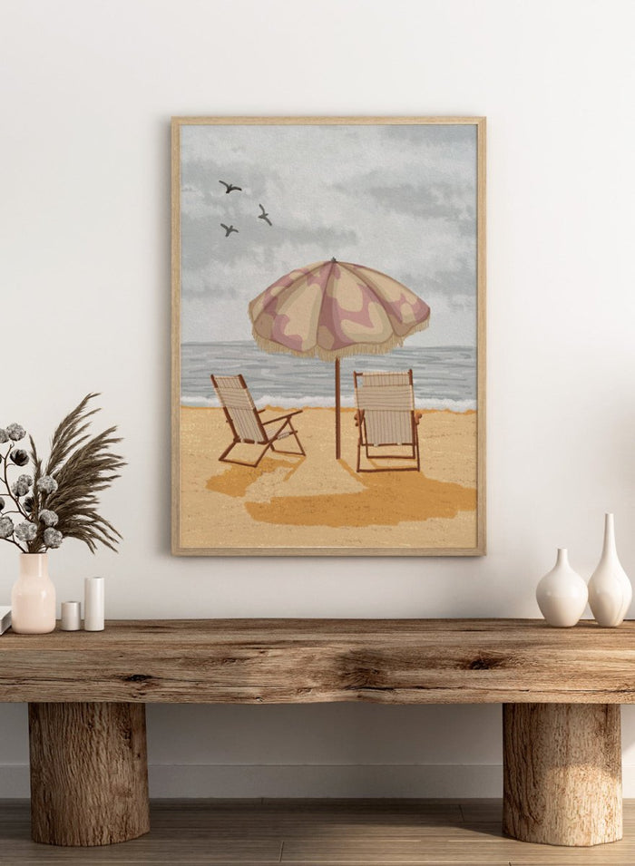 A beach scene artwork showing two wooden deck chairs under a beige and dusty pink patterned umbrella on a sandy shore, with the ocean and cloudy sky behind them. Two birds are visible in the sky. Seaside Umbrella Chairs by Lisa Solomoniuk premium framed fine art print featuring striped beach chairs beneath a fringed umbrella by the sea.