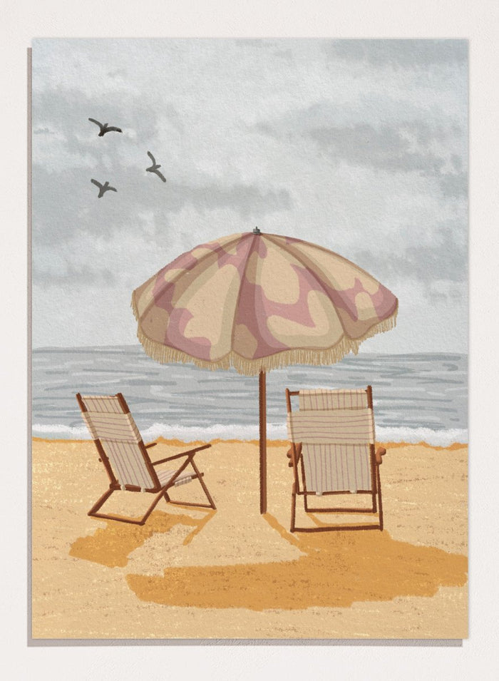 A beach scene artwork showing two wooden deck chairs under a beige and dusty pink patterned umbrella on a sandy shore, with the ocean and cloudy sky behind them. Two birds are visible in the sky. Seaside Umbrella Chairs by Lisa Solomoniuk premium framed fine art print featuring striped beach chairs beneath a fringed umbrella by the sea.