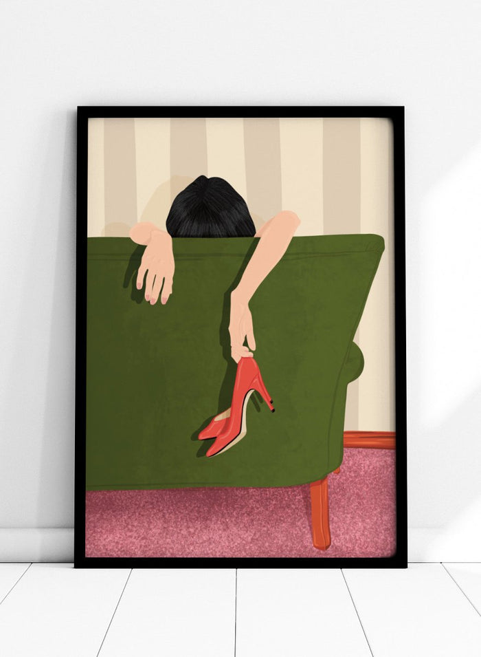 A stylized illustration of a person sitting on a green sofa, holding a pair of red high-heeled shoes. The person has dark hair and pale skin, with striped beige walls and a pink carpet in the background. Woman Resting Red Heels by Lisa Solomoniuk premium framed fine art print featuring a woman draped over a green chair holding bright red heels.