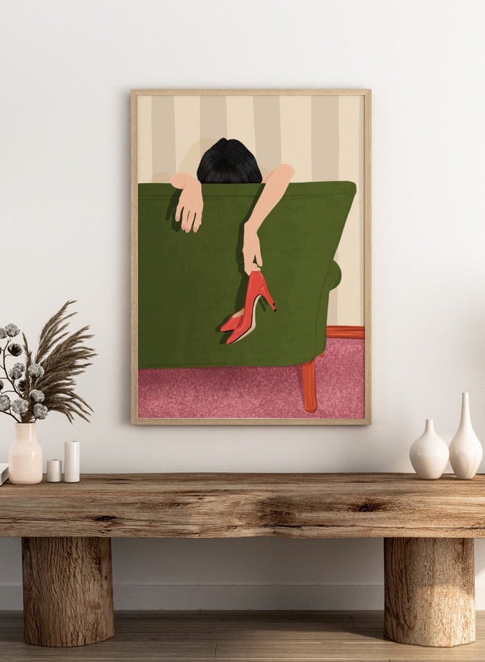 A stylized illustration of a person sitting on a green sofa, holding a pair of red high-heeled shoes. The person has dark hair and pale skin, with striped beige walls and a pink carpet in the background. Woman Resting Red Heels by Lisa Solomoniuk premium framed fine art print featuring a woman draped over a green chair holding bright red heels.
