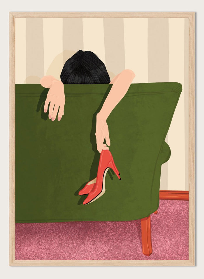 A stylized illustration of a person sitting on a green sofa, holding a pair of red high-heeled shoes. The person has dark hair and pale skin, with striped beige walls and a pink carpet in the background. Woman Resting Red Heels by Lisa Solomoniuk premium framed fine art print featuring a woman draped over a green chair holding bright red heels.
