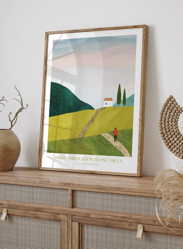 Illustration of a person walking along a path through rolling hills with a house and trees in the background. Path Through Rolling Hills by Longwayhome is a minimalist landscape art print featuring rolling green hills, countryside scenery, and modern travel inspired wall art.