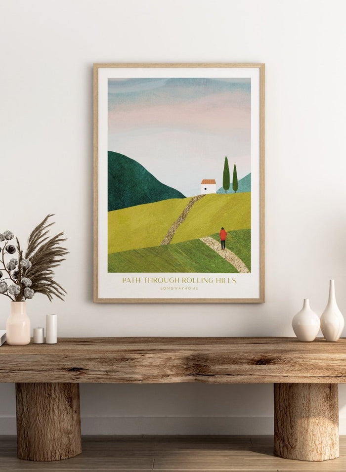 Illustration of a person walking along a path through rolling hills with a house and trees in the background. Path Through Rolling Hills by Longwayhome is a minimalist landscape art print featuring rolling green hills, countryside scenery, and modern travel inspired wall art.
