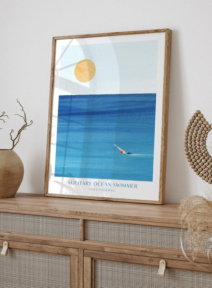 Art print of a solitary ocean swimmer with a large sun in the sky. Solitary Ocean Swimmer by Longwayhome is a minimalist ocean art print featuring deep blue water, lone swimmer imagery, and calming coastal wall art.