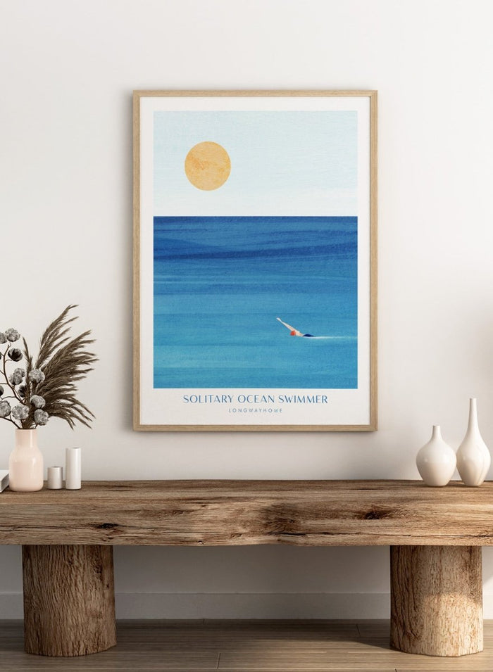 Art print of a solitary ocean swimmer with a large sun in the sky. Solitary Ocean Swimmer by Longwayhome is a minimalist ocean art print featuring deep blue water, lone swimmer imagery, and calming coastal wall art.