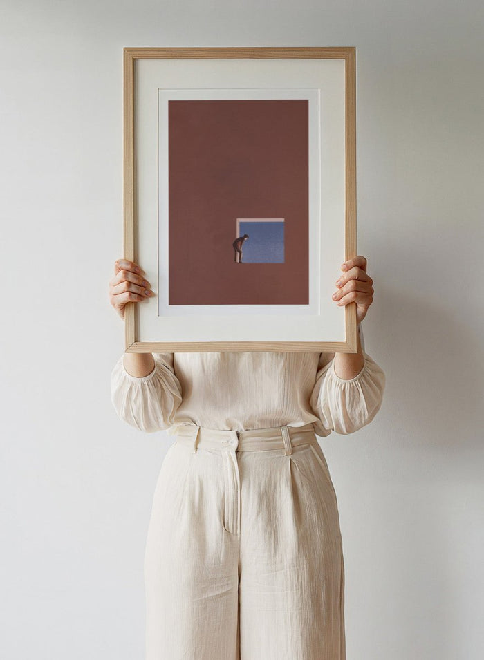 Curiosity by Maarten Léon is a minimalist collage art print showing a figure peering into a blue opening, exploring themes of curiosity and quiet discovery.