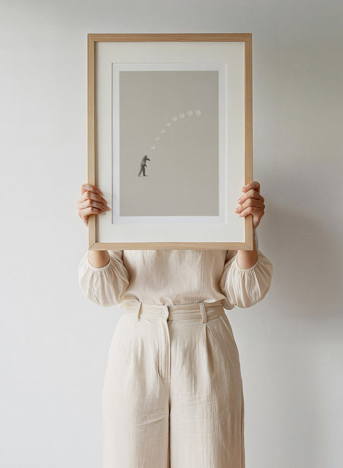 Man throwing the moon across the sky in Lucky Shot by Maarten Léon. Surreal collage wall art, minimalist contemporary poster, premium fine art with real wood frame.