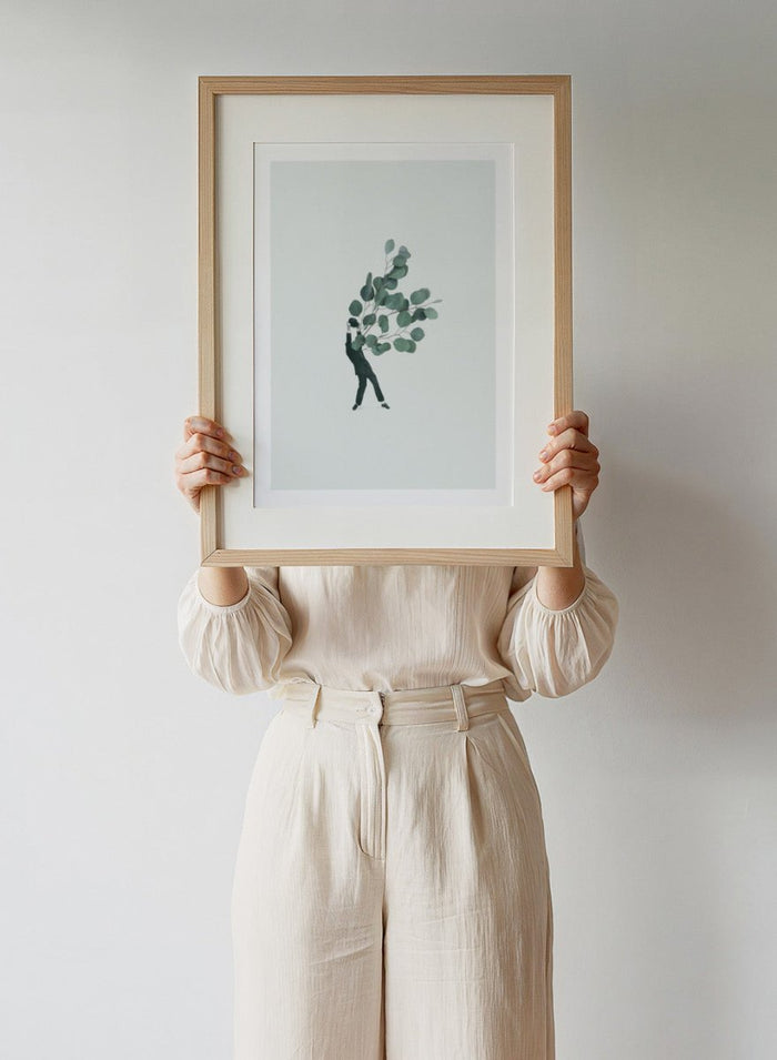 The Extravert by Maarten Léon collage art print showing a figure holding oversized eucalyptus branches. Premium fine art print with real wood framing.