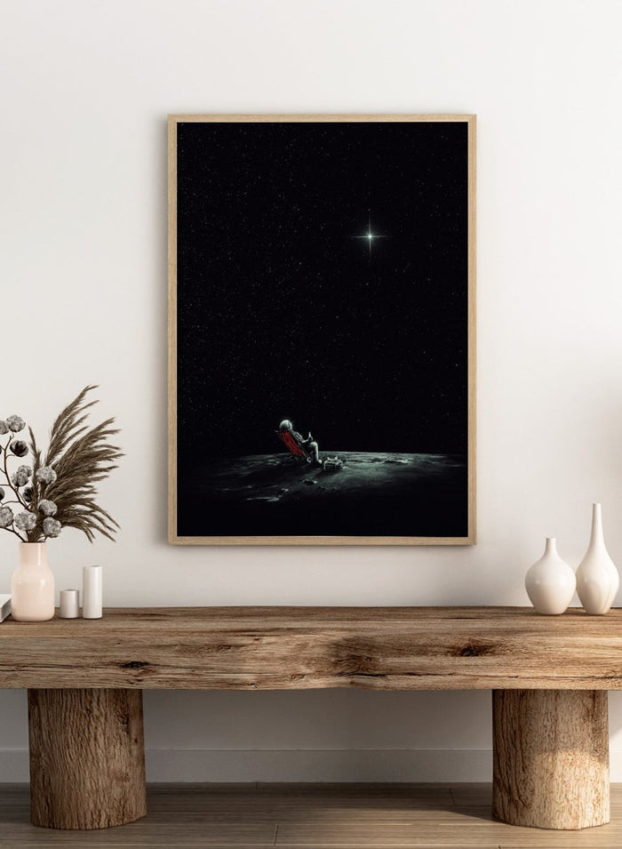 Person sitting on a chair under a starry sky. Astronaut Star Gazer by Nicebleed is a surreal space art print featuring a lone astronaut under a star-filled sky, modern aesthetic wall poster.
