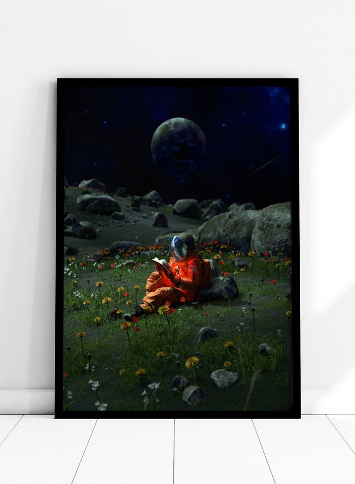 Person in orange spacesuit sitting on the moon reading a book with a large moon and stars in the background. Astronaut’s Alien Garden by Nicebleed is a surreal space art print featuring an astronaut reading in a floral alien landscape, modern aesthetic wall poster.