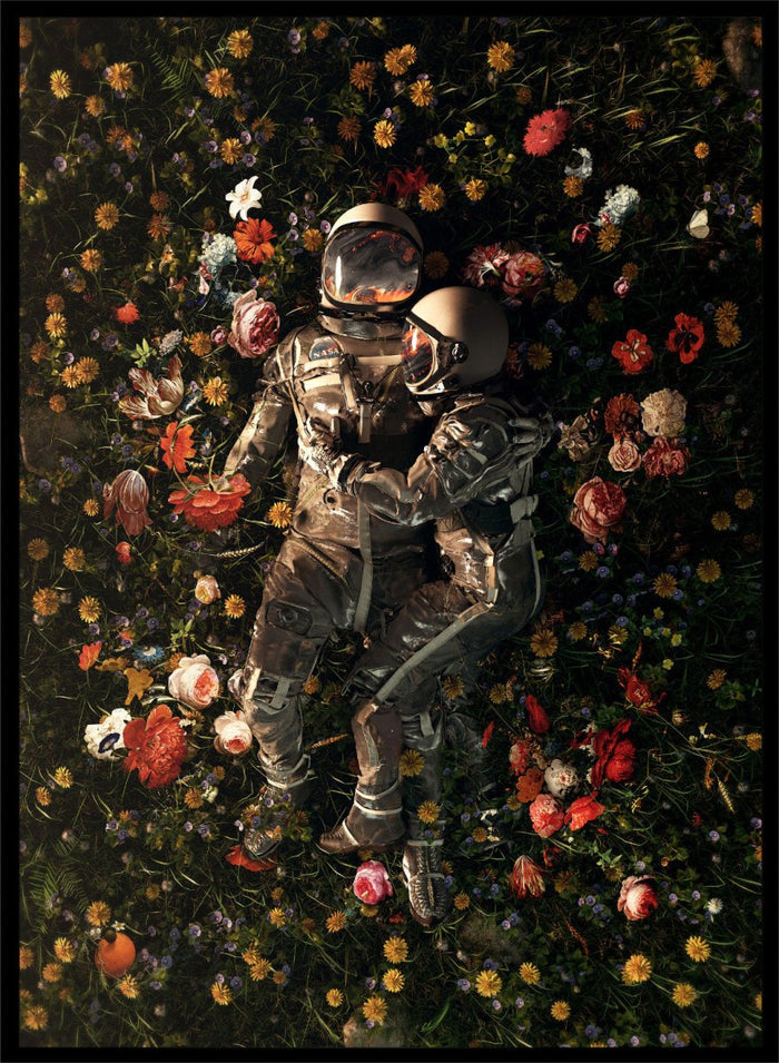 Astronaut lying on a bed of flowers with a dark background. Cosmic Couple Bloom by Nicebleed is a surreal astronaut floral art print featuring two astronauts in a field of flowers, modern aesthetic wall poster.