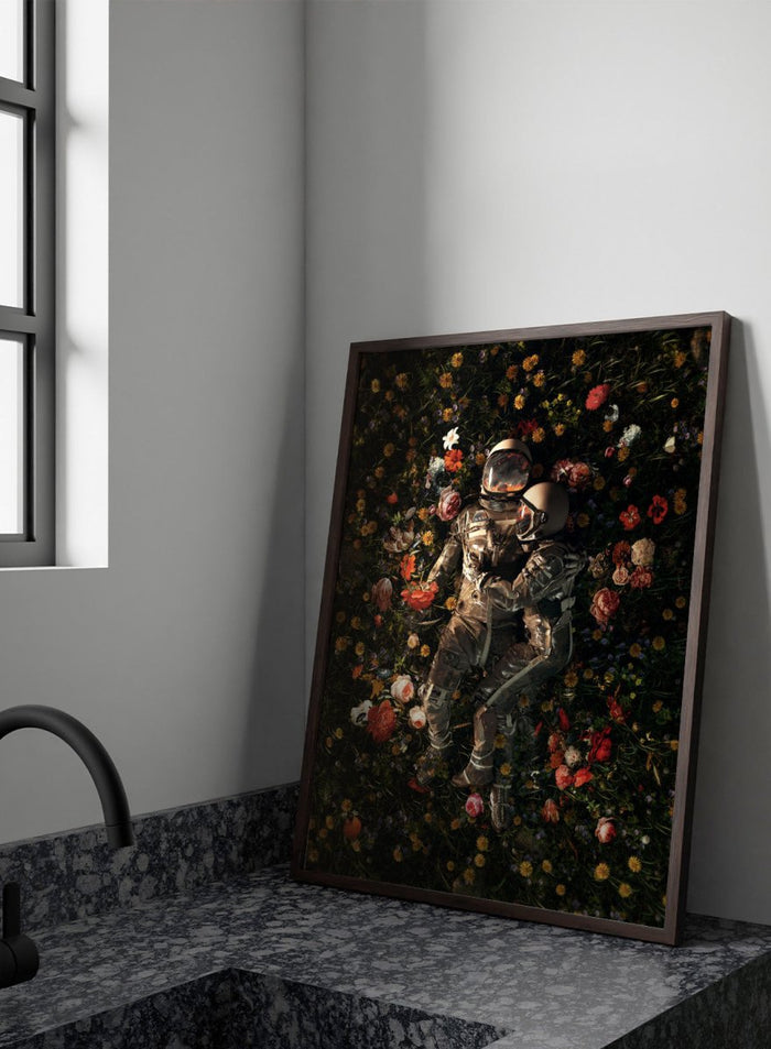Astronaut lying on a bed of flowers with a dark background. Cosmic Couple Bloom by Nicebleed is a surreal astronaut floral art print featuring two astronauts in a field of flowers, modern aesthetic wall poster.