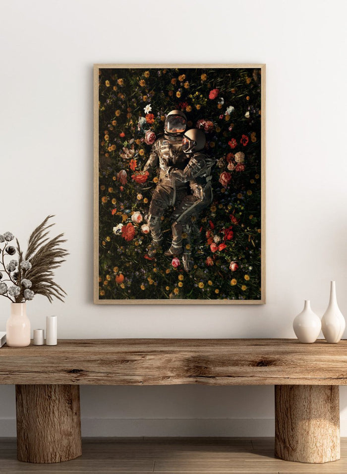 Astronaut lying on a bed of flowers with a dark background. Cosmic Couple Bloom by Nicebleed is a surreal astronaut floral art print featuring two astronauts in a field of flowers, modern aesthetic wall poster.