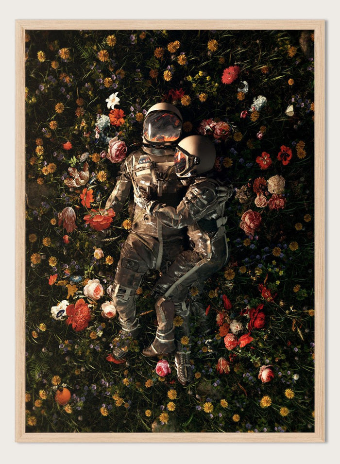 Astronaut lying on a bed of flowers with a dark background. Cosmic Couple Bloom by Nicebleed is a surreal astronaut floral art print featuring two astronauts in a field of flowers, modern aesthetic wall poster.