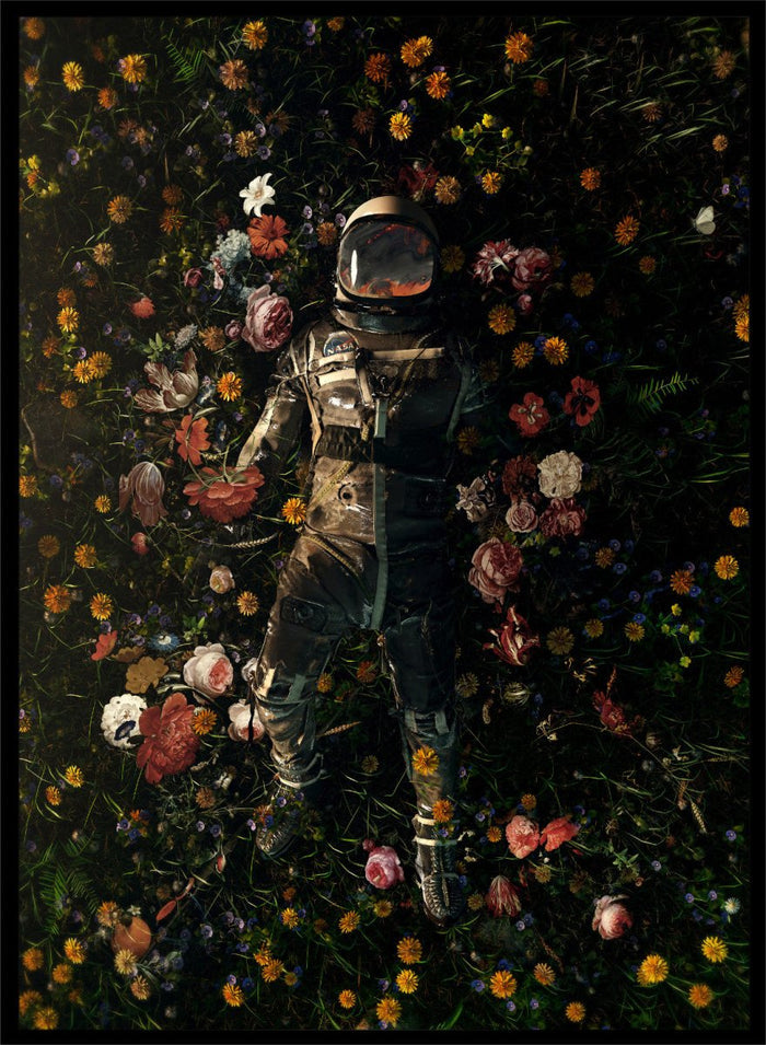 Person in a spacesuit lying on a bed of flowers with a dark background. Cosmic Floral Dream by Nicebleed is a surreal astronaut floral art print featuring a space figure surrounded by flowers, modern aesthetic wall poster.