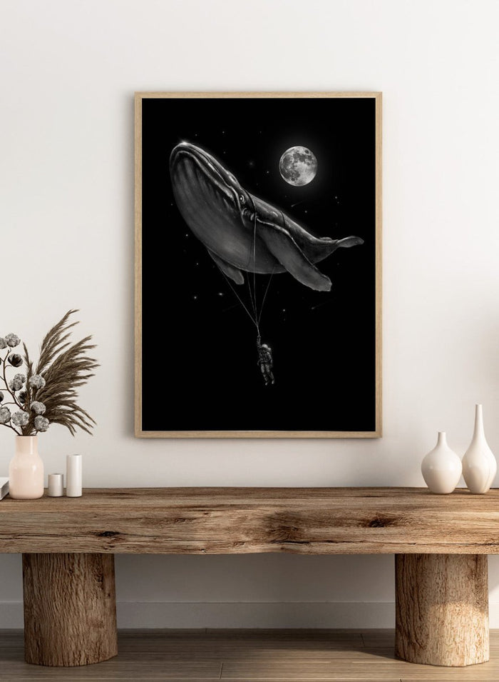 Black and white illustration of a large whale balloon with a person attached, set against a starry night sky with a moon. Cosmic Whale Ride by Nicebleed is a surreal space art print featuring an astronaut hanging from a floating whale, modern aesthetic wall poster.