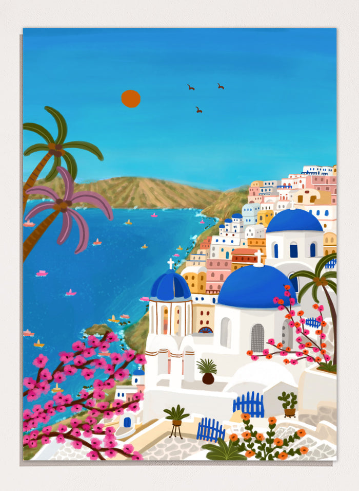 Shop Santorini Blue Domes by Nidhi Kachhadiya, a colorful Greek island wall art print inspired by Santorini, blue domes, whitewashed architecture, and Mediterranean views. A colorful illustrated coastal village scene with white buildings, bright blue domes, palm trees, pink flowering branches, a blue sea, and a clear sky with a sun and birds.