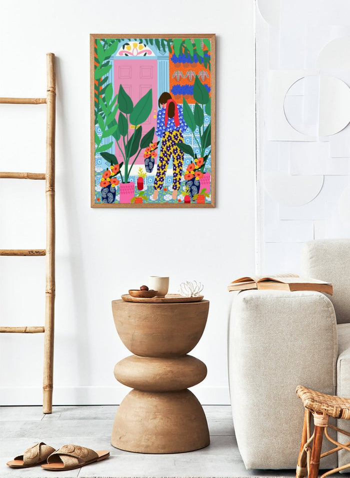 Illustration of a person in colorful pants standing in front of a pink door with plants and flowers. Floral Oasis Retreat by Rafaela Mascaro art print featuring woman in lush garden doorway, colorful plants, patterned tiles, and vibrant contemporary botanical wall art poster.