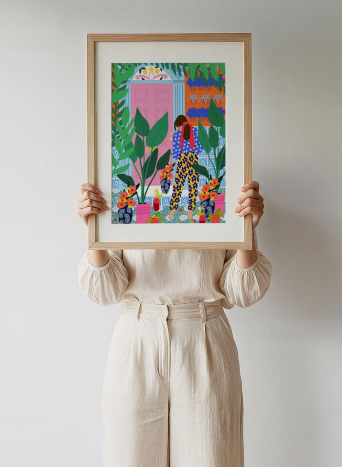 Illustration of a person in colorful pants standing in front of a pink door with plants and flowers. Floral Oasis Retreat by Rafaela Mascaro art print featuring woman in lush garden doorway, colorful plants, patterned tiles, and vibrant contemporary botanical wall art poster.