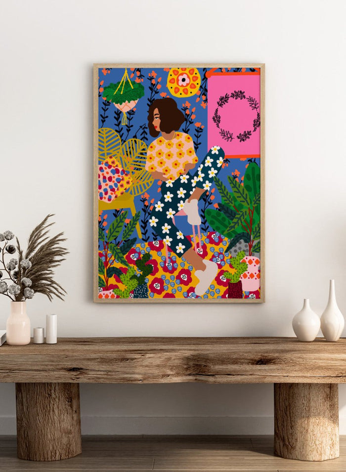 Colorful illustration of a woman sitting among flowers and plants with a vibrant background. Floral Retreat Girl by Rafaela Mascaro fine art print poster with seated woman, bold floral interior, botanical decor, modern contemporary aesthetic wall art.