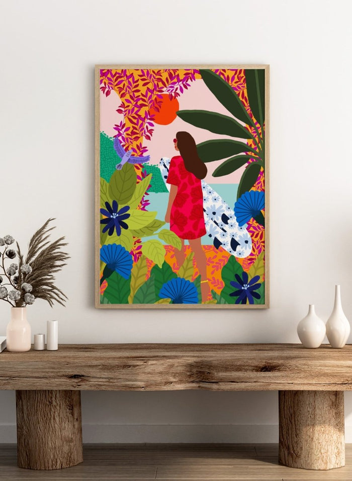 Woman in a red dress with a white surfboard amidst tropical foliage and flowers. Going Surfing by Rafaela Mascaro is a colorful tropical art print featuring a surfer, lush botanicals, vibrant florals, and sunny coastal inspiration.