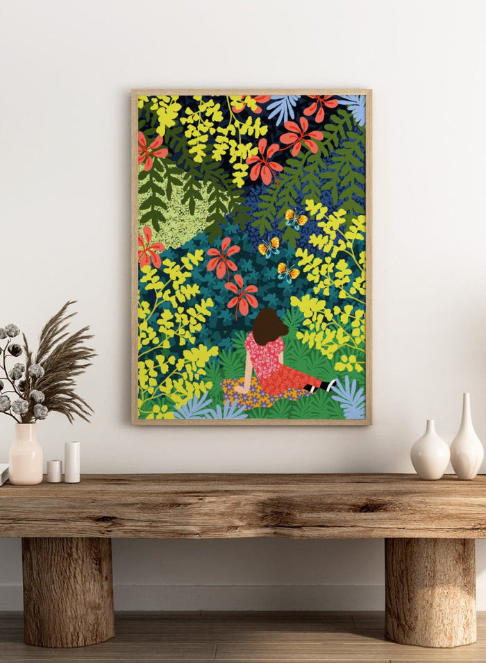 Illustration of a person sitting among colorful flowers and foliage. Picnic in the Forest by Rafaela Mascaro fine art print featuring lush botanical forest, oversized leaves, butterflies, modern colorful wall art poster.