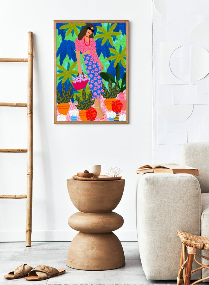 Woman in a floral dress holding a basket of flowers amidst colorful plants. Walking Between Gardens by Rafaela Mascaro fine art print poster featuring woman carrying flowers in lush tropical garden, modern contemporary botanical wall art.